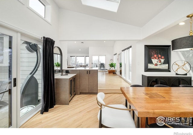 dining space featuring light wood-style flooring, a skylight, and high vaulted ceiling