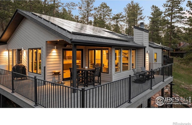 back of house featuring a shingled roof and solar panels