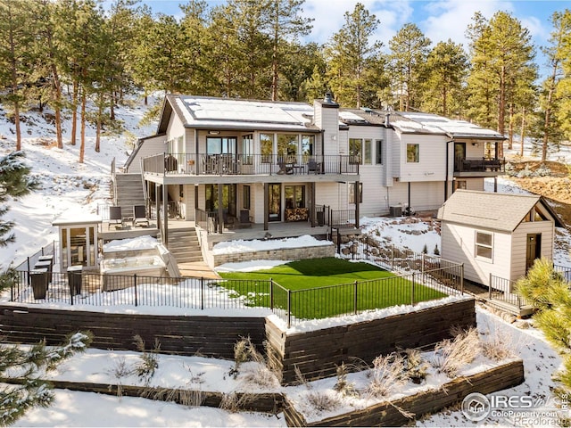 snow covered house with a yard, a fenced backyard, an outdoor structure, a patio, and a chimney