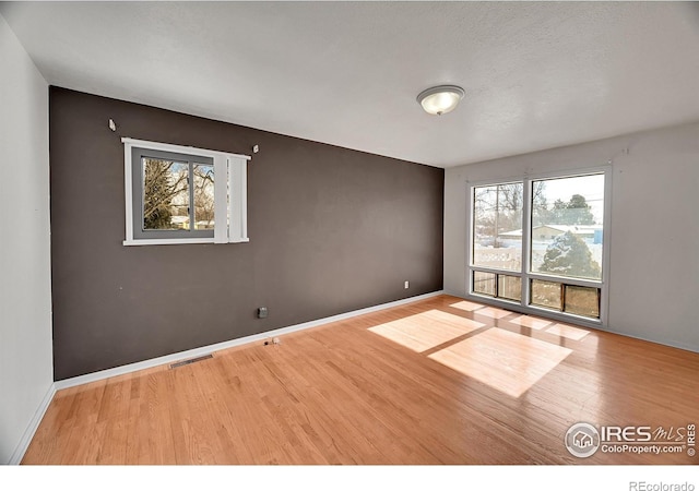 spare room with baseboards, visible vents, and wood finished floors