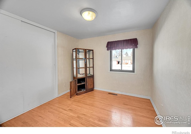 spare room featuring light wood-type flooring, visible vents, and baseboards