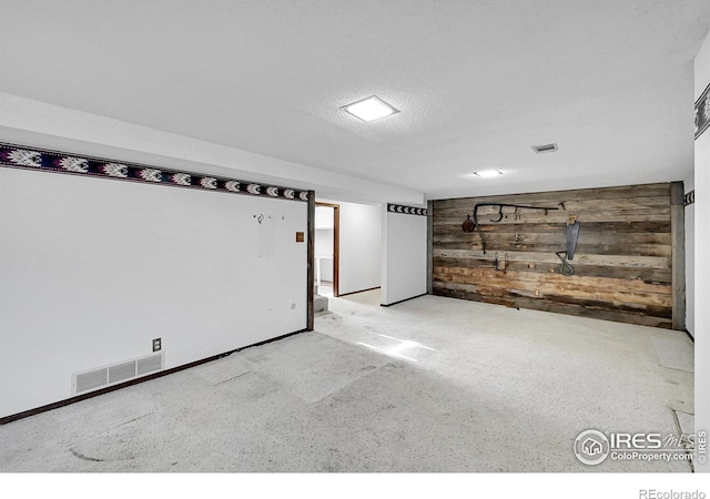 spare room featuring light carpet, wood walls, visible vents, and a textured ceiling