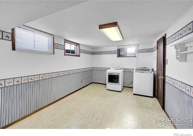 kitchen with washing machine and dryer, wainscoting, a textured ceiling, and light floors