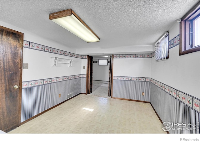 empty room featuring a wainscoted wall, visible vents, light floors, and a textured ceiling