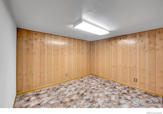 empty room with wood walls, baseboards, and carpet flooring