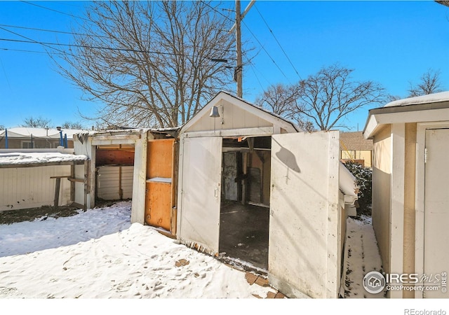 snow covered structure featuring a storage shed, fence, and an outdoor structure