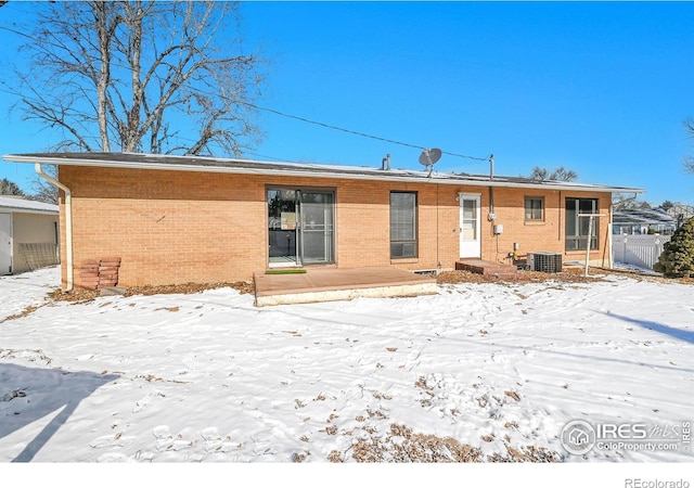 snow covered rear of property with brick siding, fence, and central AC unit