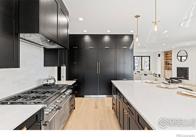 kitchen featuring cooktop, dark cabinets, range hood, and light wood-style flooring
