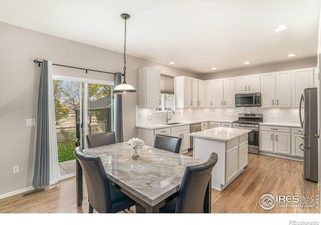 kitchen with white cabinets, a kitchen island, hanging light fixtures, stainless steel appliances, and a sink