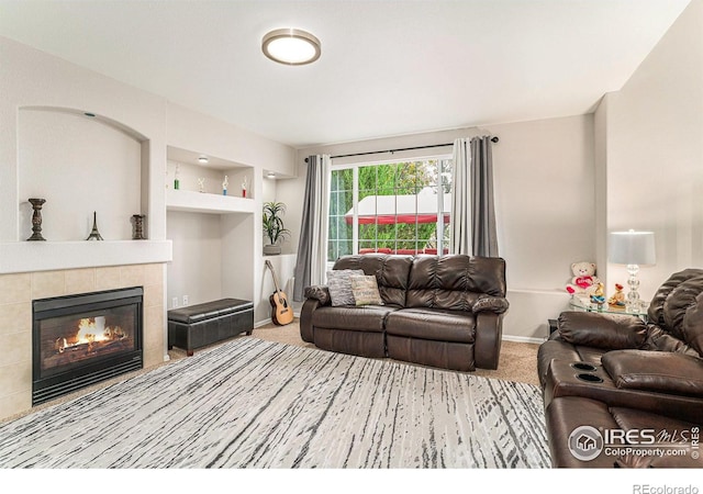 living area with built in shelves, carpet, baseboards, and a tiled fireplace