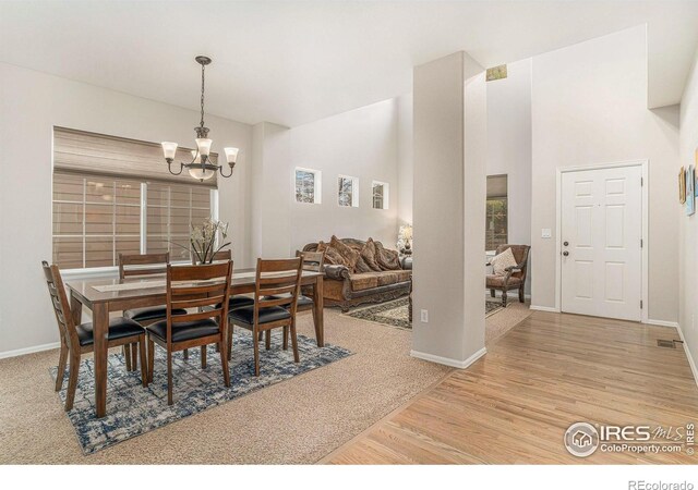 dining room with baseboards, a notable chandelier, a towering ceiling, and light wood finished floors