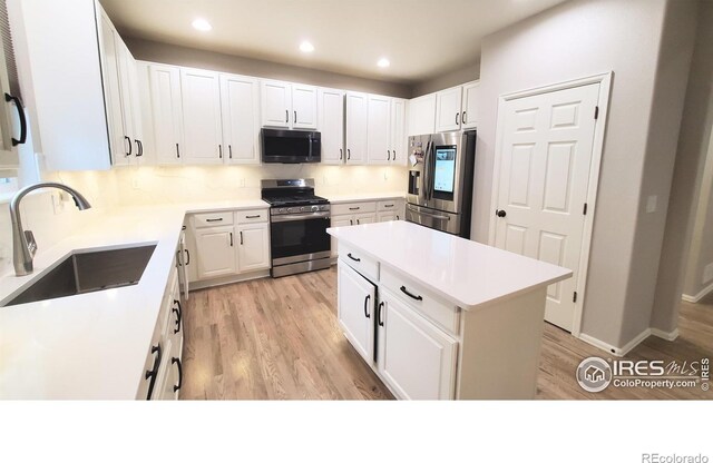 kitchen featuring stainless steel appliances, light countertops, white cabinetry, a sink, and light wood-type flooring