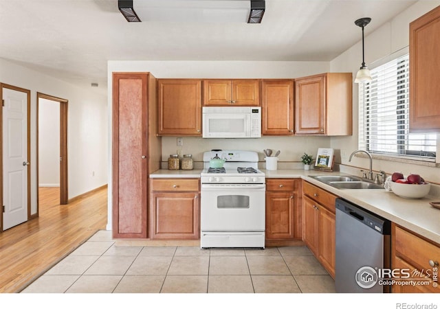 kitchen with white appliances, brown cabinets, decorative light fixtures, light countertops, and a sink