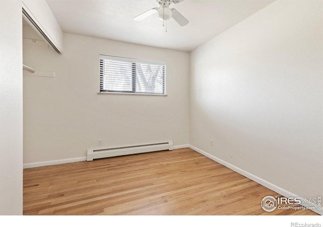 spare room featuring a baseboard heating unit, baseboards, and light wood-style floors