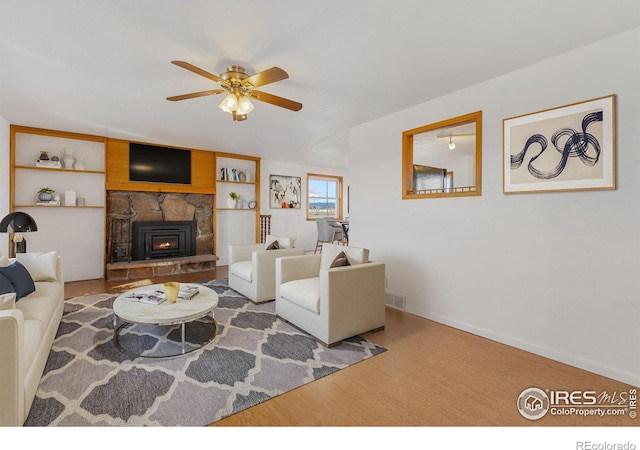 living area featuring baseboards, visible vents, a ceiling fan, and a stone fireplace