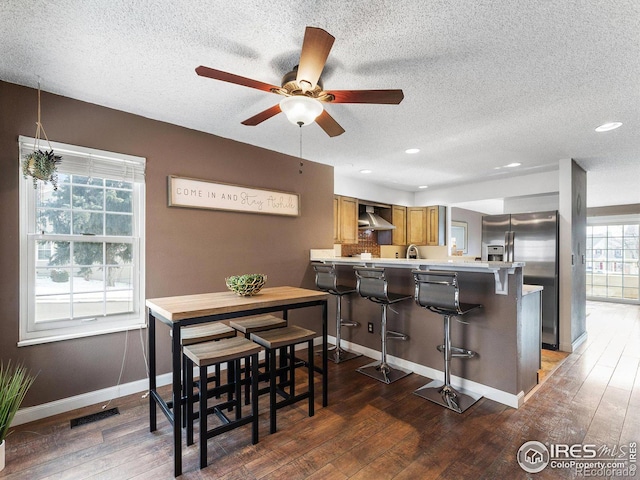 kitchen with a peninsula, wall chimney range hood, wood finished floors, and a kitchen breakfast bar