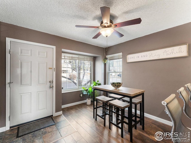 dining space with a ceiling fan, a textured ceiling, baseboards, and dark wood-style flooring