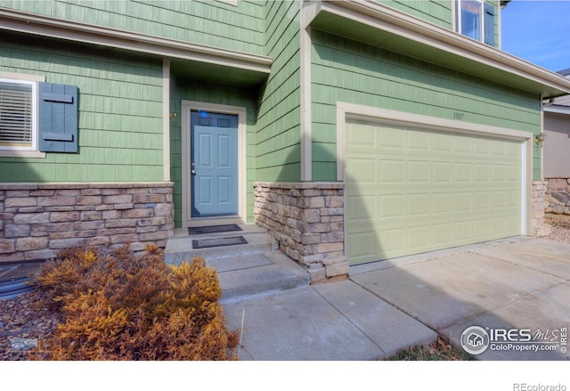 doorway to property featuring a garage, stone siding, and driveway