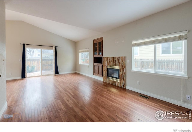 unfurnished living room with lofted ceiling, wood finished floors, a glass covered fireplace, and visible vents