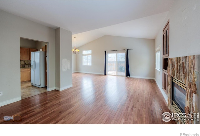 unfurnished living room featuring vaulted ceiling, a notable chandelier, a fireplace, and light wood-style flooring