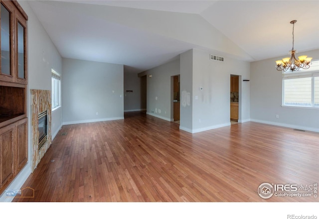 unfurnished living room with lofted ceiling, wood finished floors, a glass covered fireplace, and an inviting chandelier