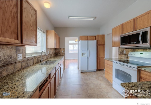 kitchen with light tile patterned floors, light stone counters, white appliances, a sink, and decorative backsplash