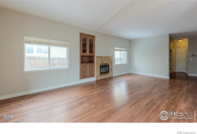 unfurnished living room with visible vents, baseboards, wood finished floors, vaulted ceiling, and a high end fireplace