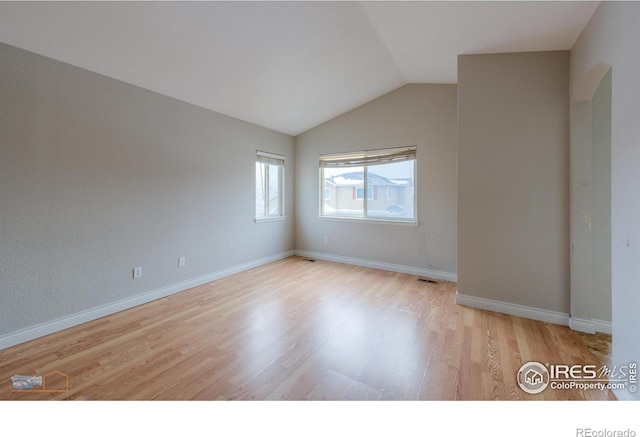 empty room featuring arched walkways, visible vents, light wood-style floors, vaulted ceiling, and baseboards