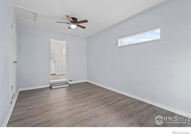 empty room featuring dark wood finished floors, visible vents, attic access, ceiling fan, and baseboards