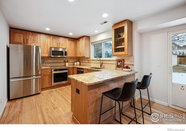 kitchen with stainless steel appliances, a peninsula, a sink, visible vents, and glass insert cabinets