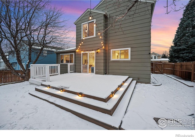 snow covered house with fence and a wooden deck