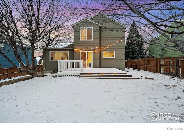 snow covered rear of property featuring a fenced backyard and a wooden deck