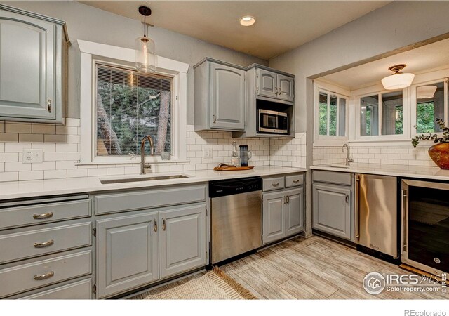 kitchen featuring beverage cooler, a sink, light countertops, appliances with stainless steel finishes, and gray cabinets