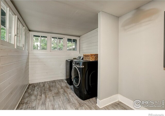 clothes washing area with light wood finished floors, laundry area, washer and clothes dryer, and wood walls