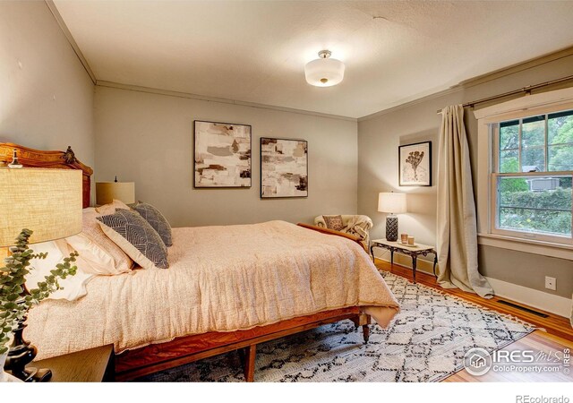 bedroom with baseboards, wood finished floors, visible vents, and crown molding