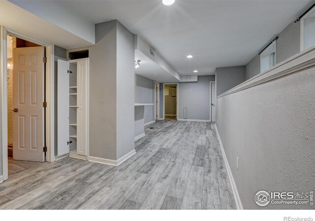 hall featuring baseboards, a textured wall, and light wood finished floors