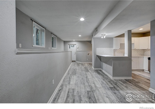 interior space featuring light countertops, light wood-style flooring, backsplash, white cabinets, and baseboards