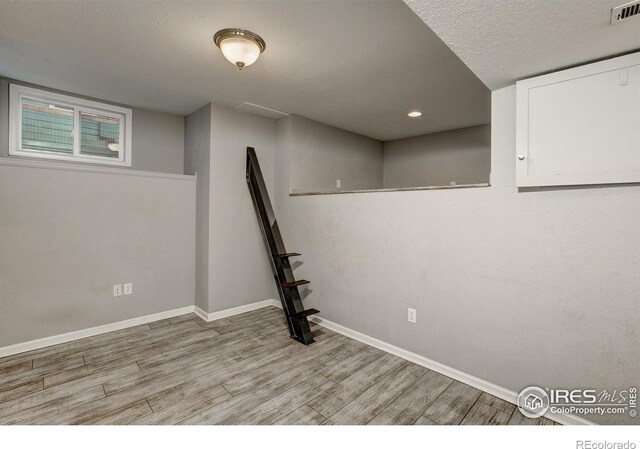 finished basement with light wood-type flooring, baseboards, visible vents, and a textured ceiling