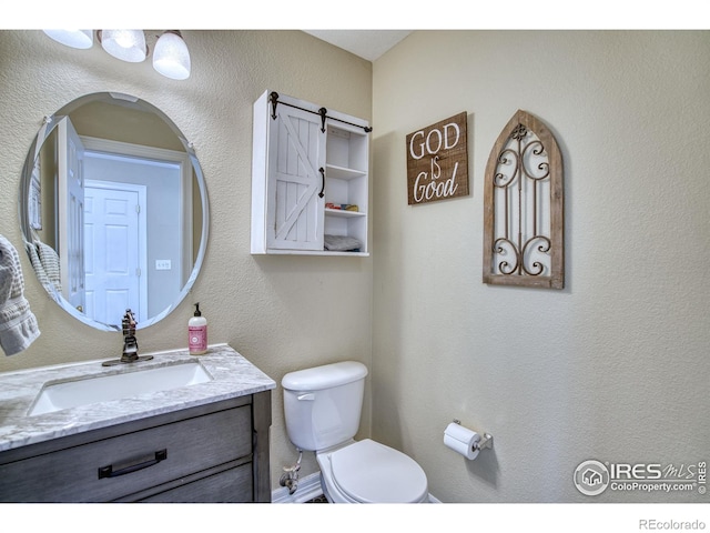 half bathroom featuring a textured wall, vanity, and toilet