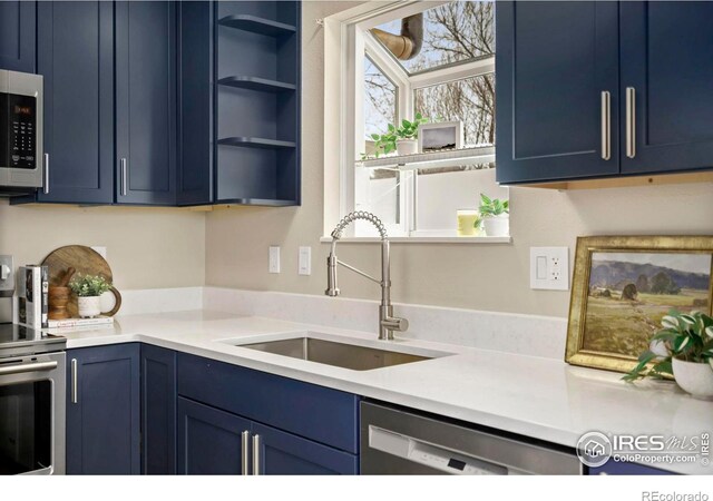 kitchen featuring blue cabinets, a sink, light countertops, appliances with stainless steel finishes, and open shelves