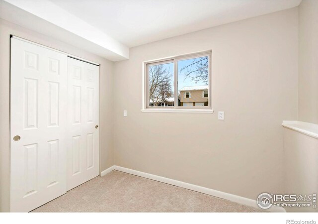 unfurnished bedroom featuring baseboards, a closet, and light colored carpet