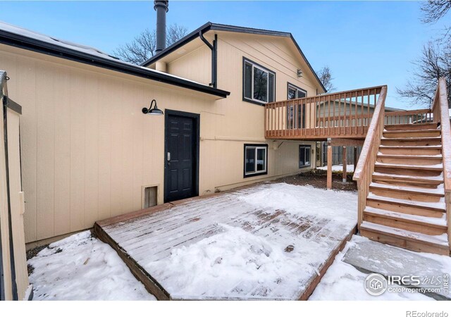 snow covered back of property featuring a deck and stairway