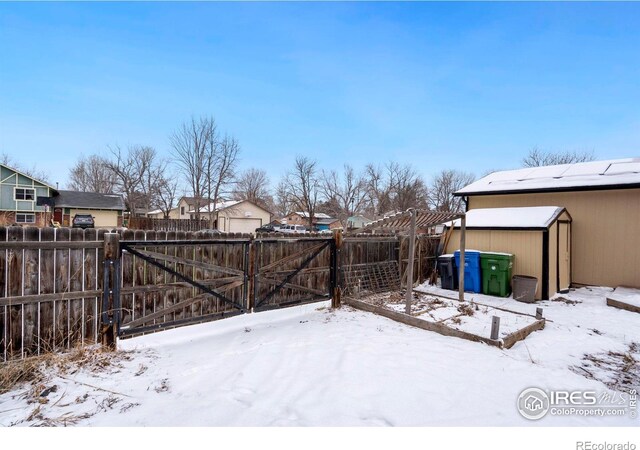 yard layered in snow with a storage unit, a gate, fence, and a residential view