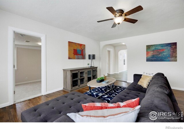 living room featuring arched walkways, dark wood-style flooring, ceiling fan, and baseboards