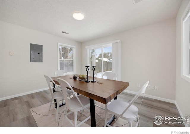 dining room featuring visible vents, light wood finished floors, electric panel, and baseboards