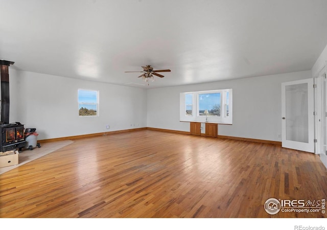 unfurnished living room with a ceiling fan, a wealth of natural light, a wood stove, and wood finished floors