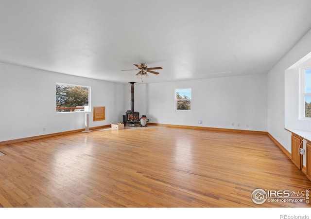 unfurnished living room featuring a wood stove, light wood finished floors, baseboards, and a healthy amount of sunlight