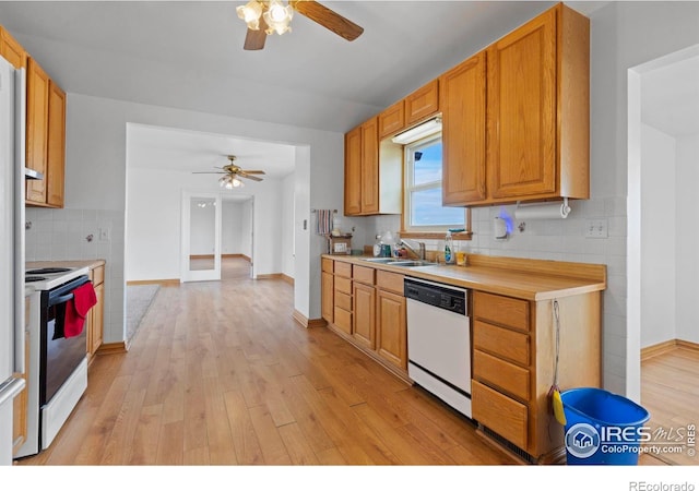 kitchen featuring white appliances, light wood finished floors, backsplash, light countertops, and a sink