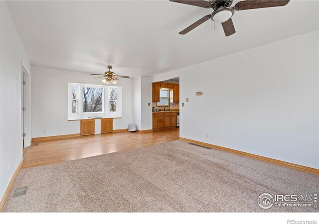 unfurnished living room with baseboards, light wood finished floors, visible vents, and light colored carpet