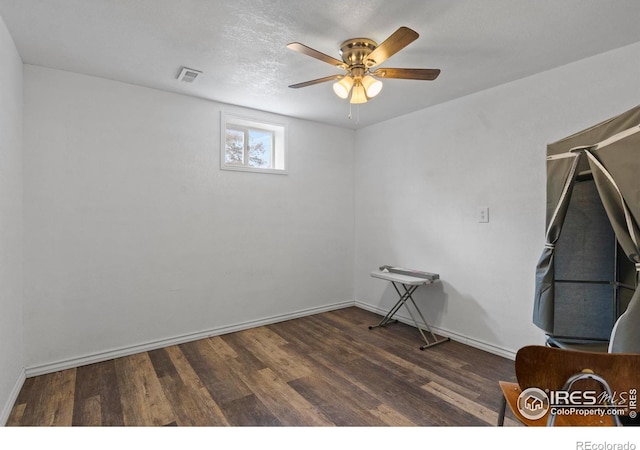 empty room featuring baseboards, visible vents, a ceiling fan, dark wood-type flooring, and a textured ceiling